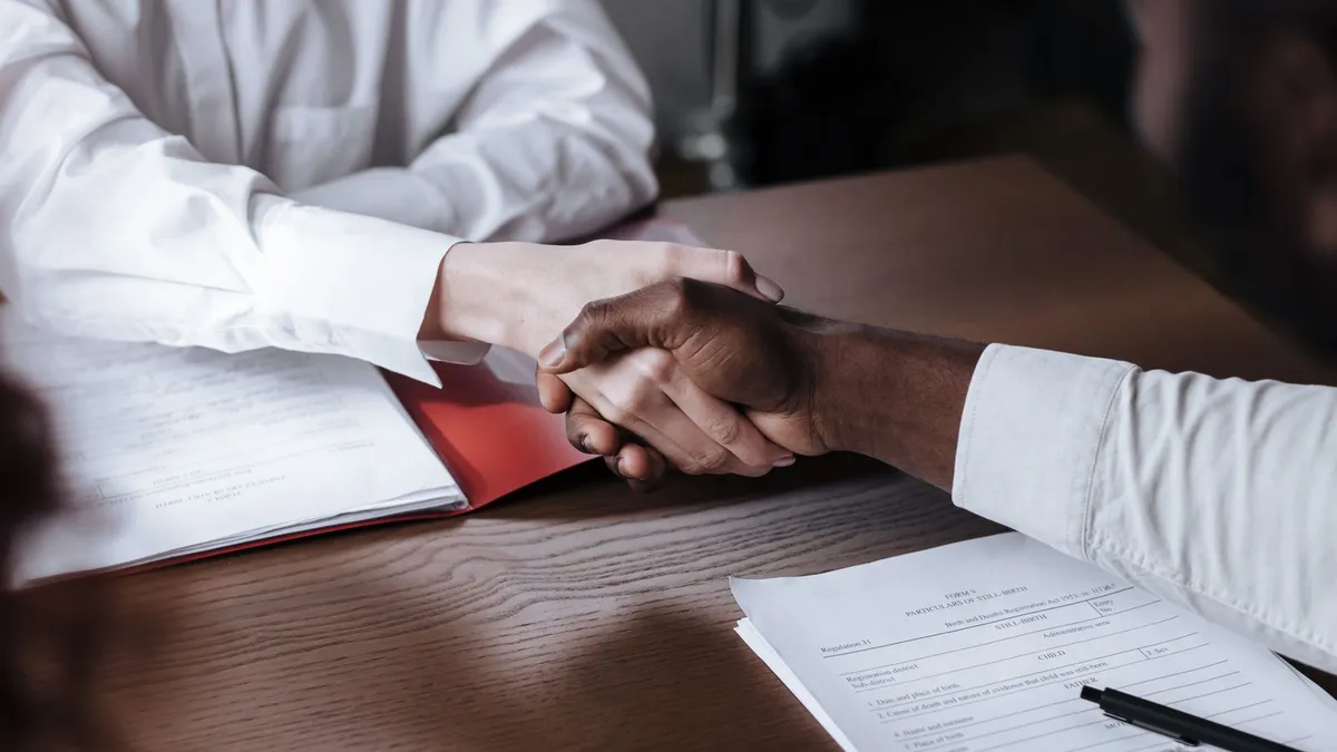 Two people shaking hands across an office desk after signing a loan guarantee