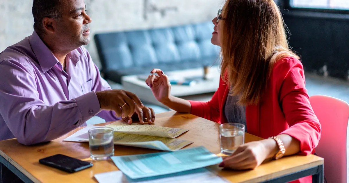 Two friends at a table discussing whether one will back the other's application for guarantor loans in Canada