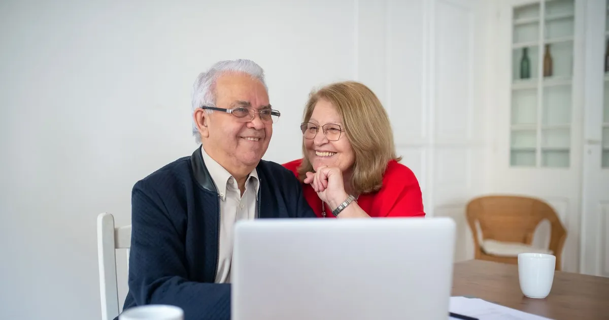 Senior couple at their kitchen table comparing pension loans on a laptop